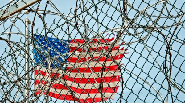 American flag in background; barbed wire in foreground