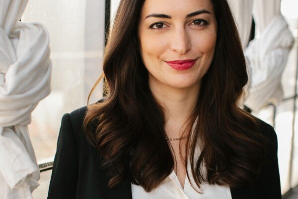 Kate smiling while wearing a white collared shirt and black blazer while in front of a window