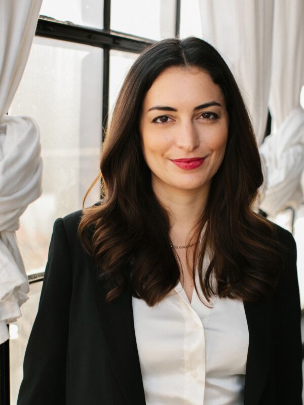 Kate smiling while wearing a white collared shirt and black blazer while in front of a window