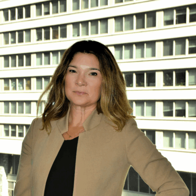 A picture of Rebecca in front of a window with a brown blazer, black shirt, and highlighted brunette and blonde hair.