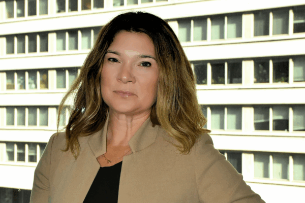 A picture of Rebecca in front of a window with a brown blazer, black shirt, and highlighted brunette and blonde hair.