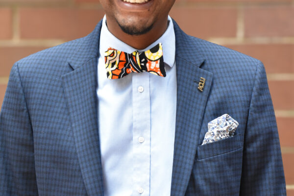A photo of Mike Lee, smiling, with a light blue button down and dark blue suit blazer with a kente cloth bowtie.