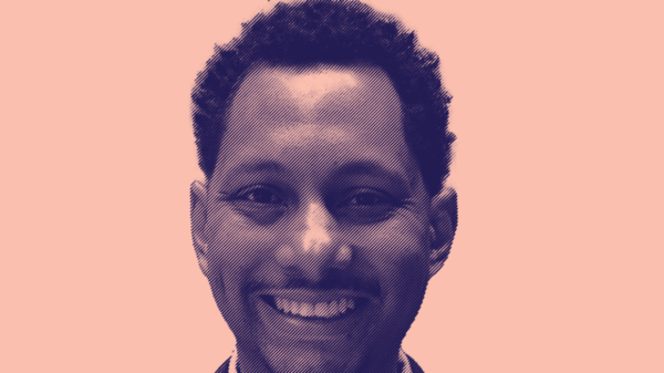 A picture of Mike Lee on a pink background smiling in navy suit and white button down