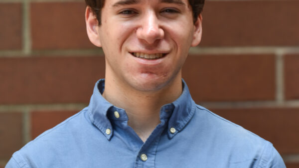 A picture of Jack Starobin on a brick wall with brown hair and a light blue polo button down