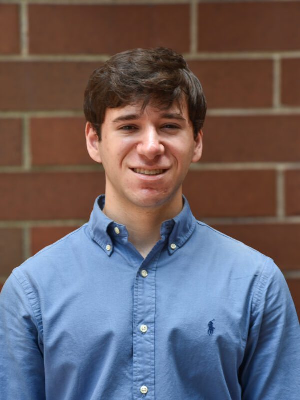 A picture of Jack Starobin on a brick wall with brown hair and a light blue polo button down