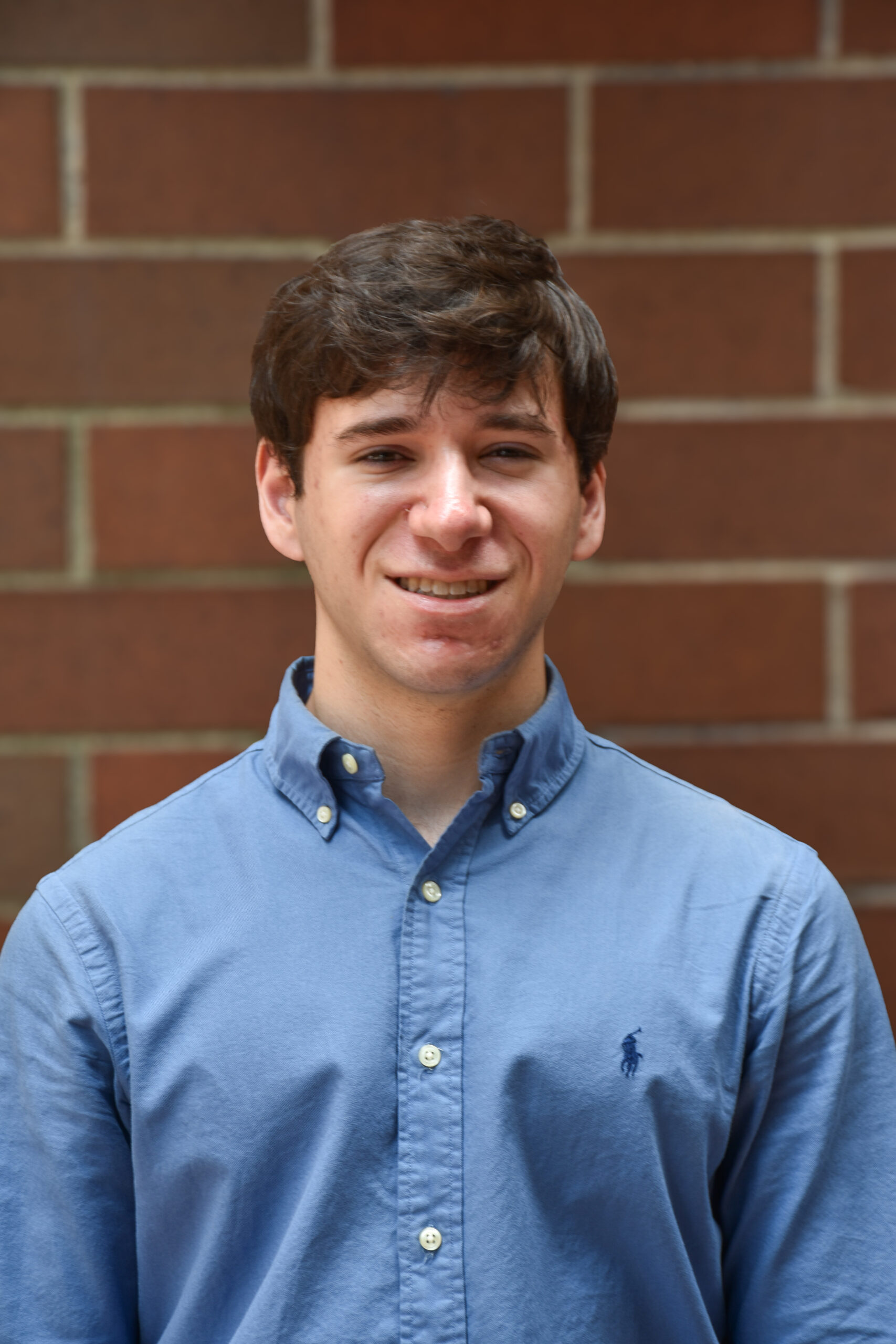 A picture of Jack Starobin on a brick wall with brown hair and a light blue polo button down