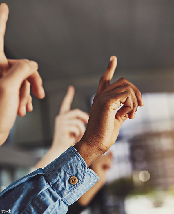 Several hands raising, one of which belongs to a Black person.