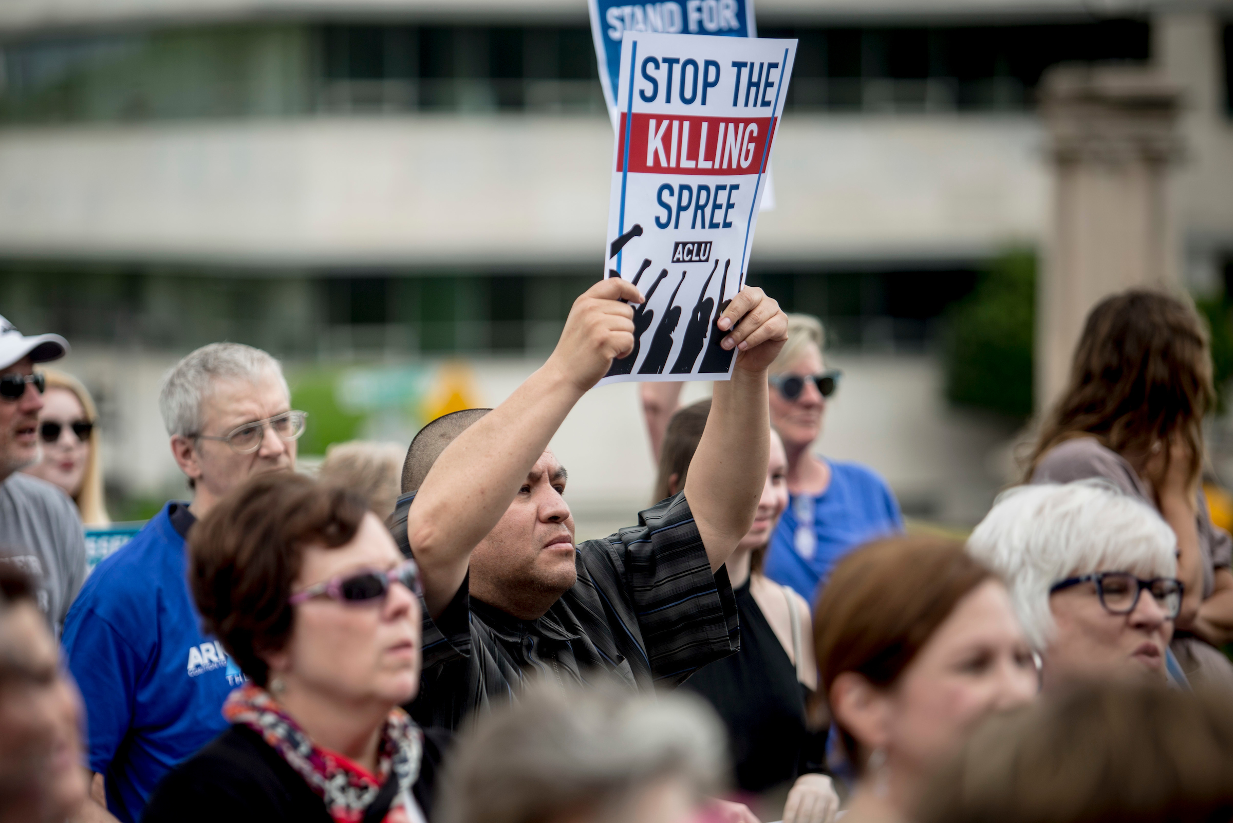 A person holding up a sign that says "Stop the killing spree".
