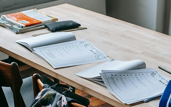 Open books on a wood desk with chairs on a green and white backpack.