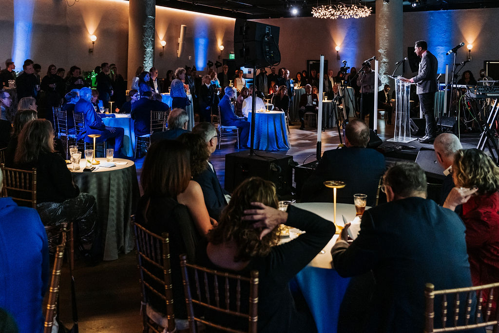 A group of people sitting at white cloth tables at an event.