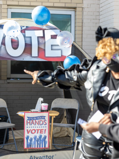 Two women pointing at a "Vote" sign outside of a polling station.