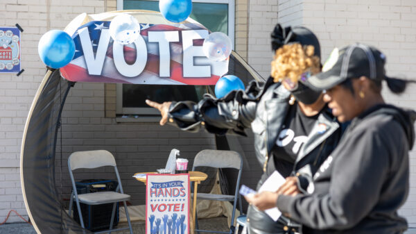 Two women pointing at a "Vote" sign outside of a polling station.