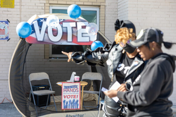Two women pointing at a "Vote" sign outside of a polling station.