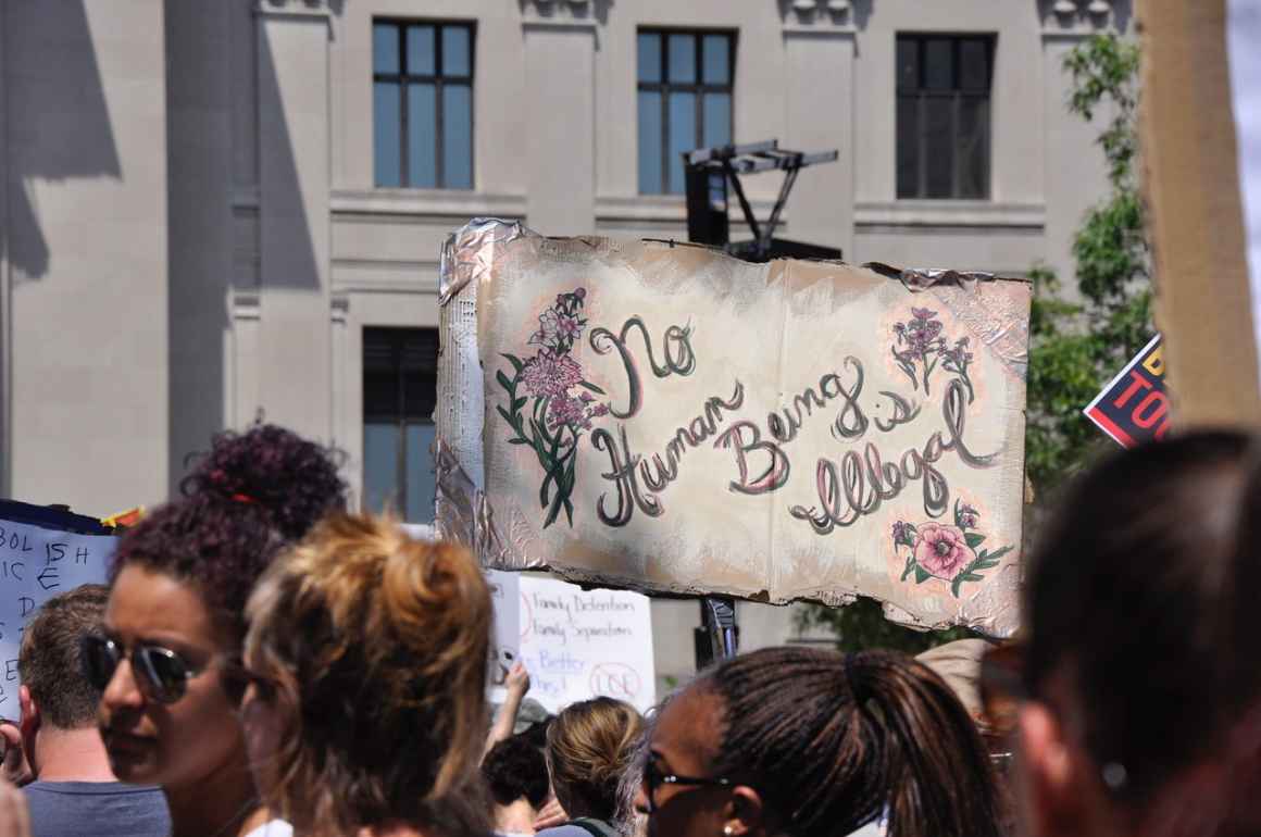 crowd of people and sign that reads 'No Human Being is Illegal'