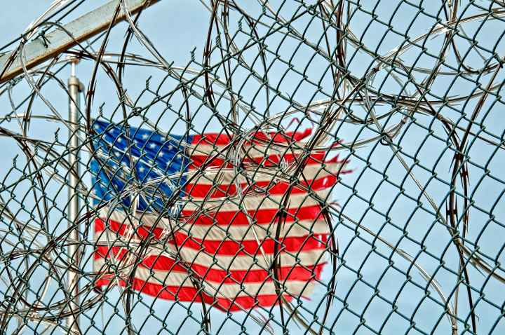 American flag in background; barbed wire in foreground