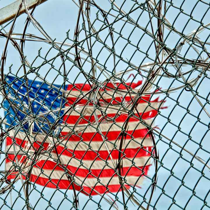 American flag in background; barbed wire in foreground